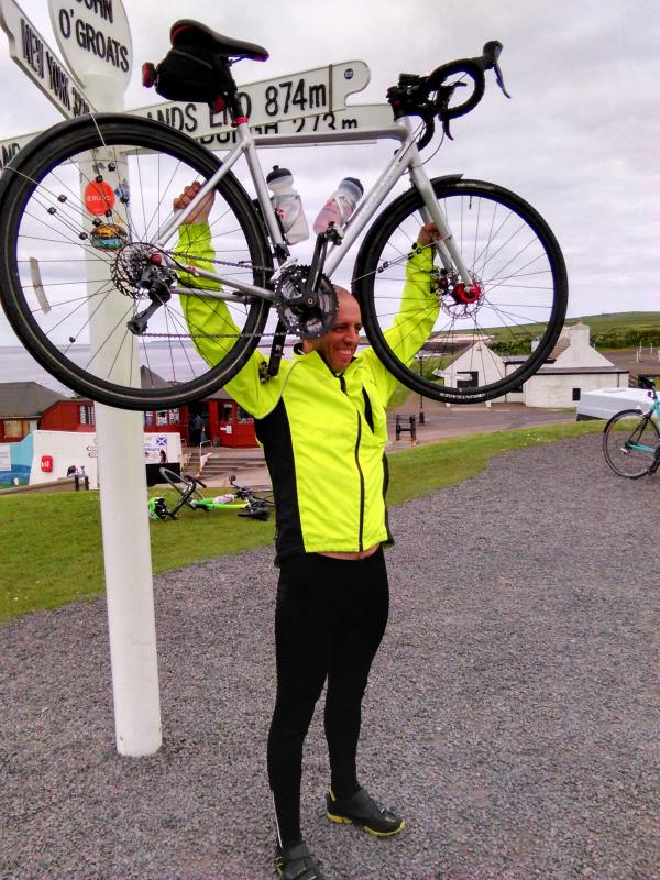 Daniel brandishing the bike up high, in jubiliation at having finally reached John O'Groats.