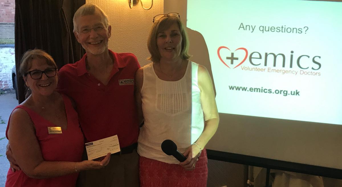 Tim presented with cheque and enveloped by joint Presidents Maggie and Jane