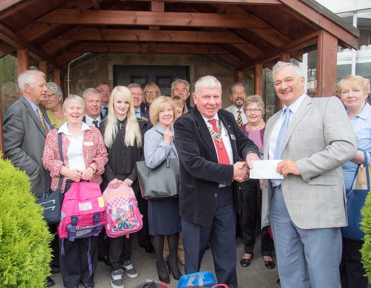 President Bill Knox presents a cheque to Mr Black of The Haven whilst Rotarians prepare to hand over backpacks to Mary's Meals.