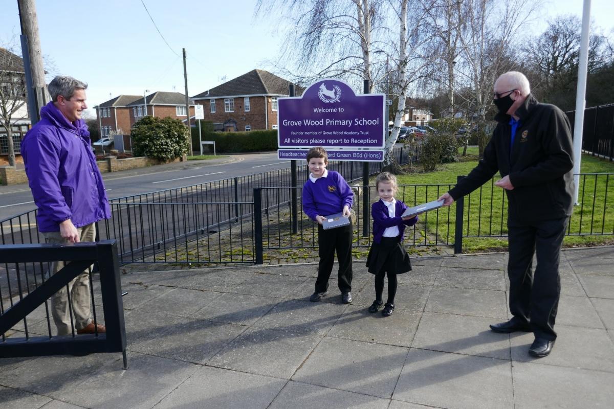 Rotary Club of Rayleigh Mill President, Rotarian Dr. Geoff Kittle, accompanied by Head Teacher Richard Green, presents laptops to two happy pupils of Grove Wood Primary School