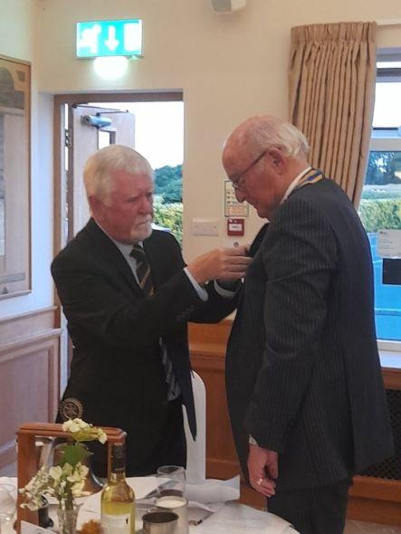 Past President Jim Nicholson pins the President Badge to new incoming president John Reid