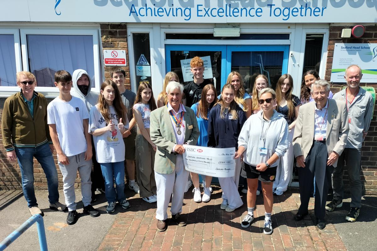President Clive Livingstone presenting the donation to teacher Rebecca Fraser watched by students and teacher Donald McDonald (far left), Rotarian Jim Anderson (2nd from right) and Glenn Dakers from World Challenge 