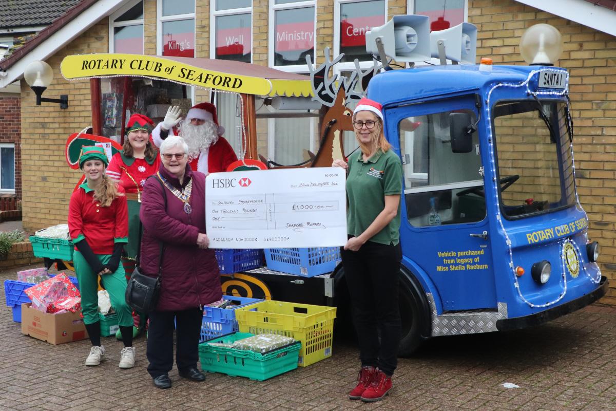 President Ann Reed presenting the donation to Dawn Woodgate, Seahaven Storehouse watched by Santa with two elves
