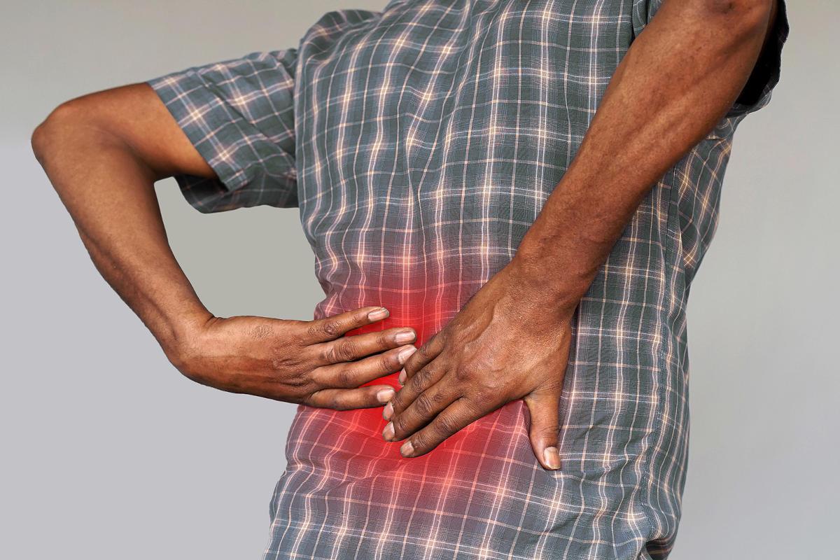 Picture of the back of a man with his hands on his painful kidneys.