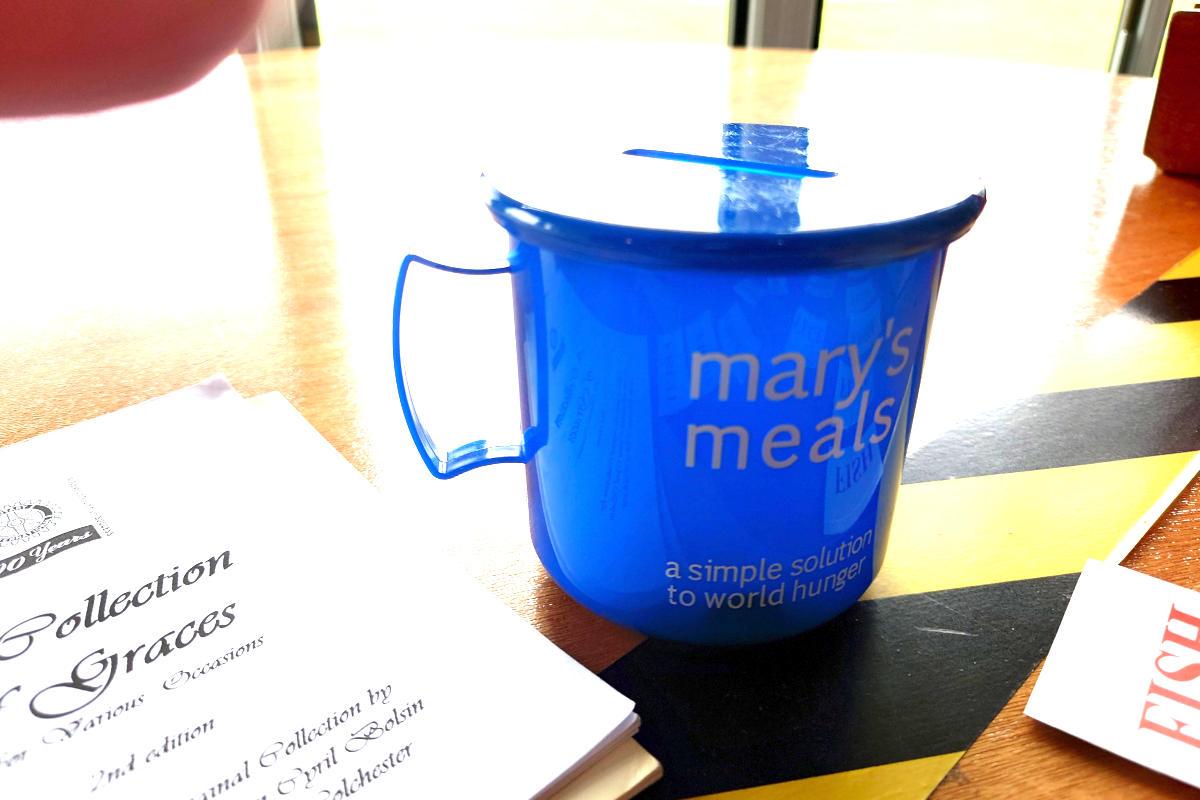 A blue cup-shaped collecting box next to a Rotary book of graces.