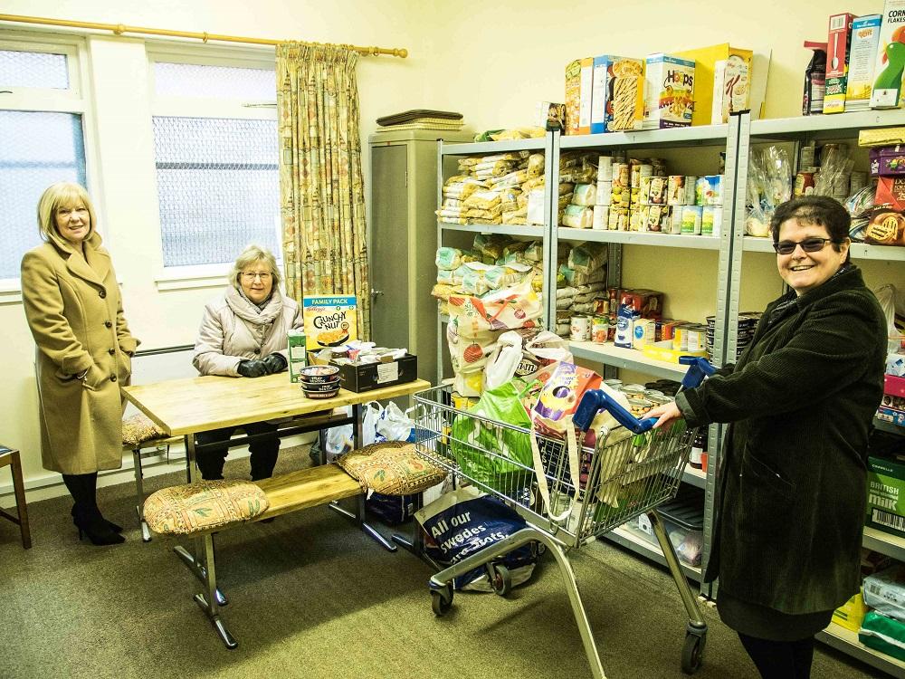 Rotarians donate to the URC Food Angel Foodbank - With the donations delivered to the Food Angels,  Betty and Elma lend a helping hand to  Rev. Branwen to restock the shelves.