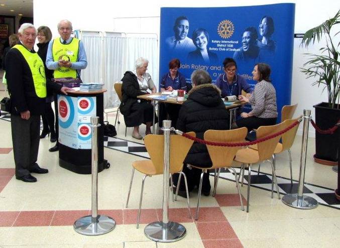 President Brian Franklin and Rotarian Keith Higgin ask for volunteers, whilst the nurses carry out checks on two ladies in front of the Rotary exhibition stand.