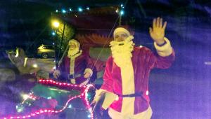 Santa collecting in the local streets at night, waves to the children. 