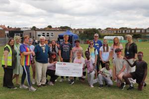 President Clive Livingstone presenting the donation to teacher Hannah Martin (in the striped top) who organised the event watched by painted students and teachers 
