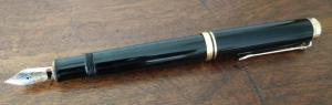 A black fountain pen resting on a wooden surface.
