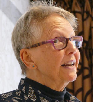 A grey-haired lady wearing glasses, viewed from her right