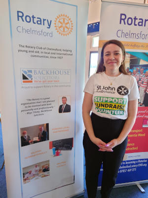 A young woman with long black hair wearing a St John's Ambulance T-shirt and standing in front of two Rotary Club banners