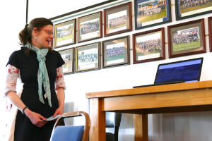 A young woman with dark hair standing by some tall tables bearing a laptop