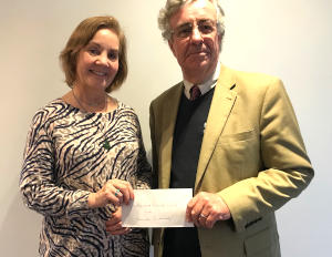 A woman with light brown hair stadning next to a man in a linen jacket and handing him an envelope