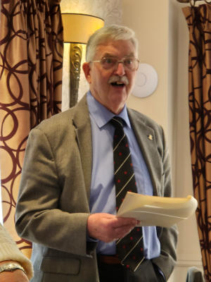 A white-haired man with glasses and a moustache and papers in his hand