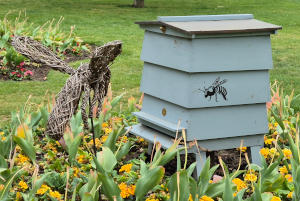 A hive with a willow sculputre of a bee arranged so that it appears to be arriving at it
