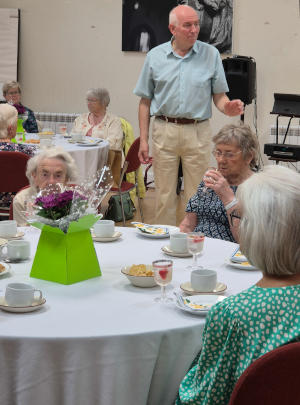 People sitting at dining tables, with a man in shiresleeves standing