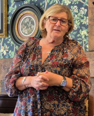 A blonde lady wearing a dark floral dress and glasses