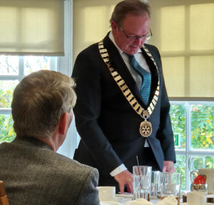 A man wearing a a District Governor's chain of office, standing by a table