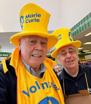 Two men wearing Marie Curie branded top hats and tabards