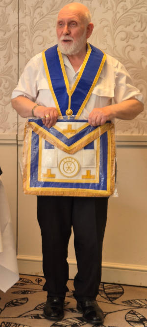 A man with a white beard wearing a Masonic collar and holding a Masonic apron