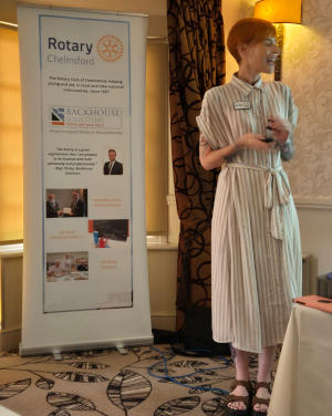 A tall lady with short red hair standing next to a Club pull-up banner