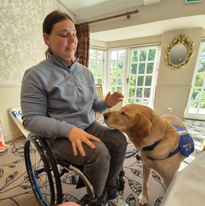 A young woman in a wheelchair with a support dog alongside her