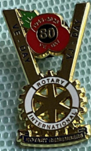 A lapel pin with a large gold V and the poppy and Rotary symbols