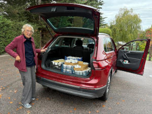 A grey-haired lady taking a box from the boot of a red car