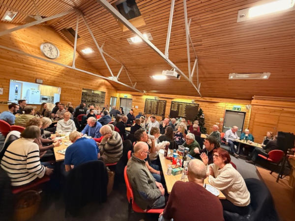 People sitting around tables in a large wooden structure