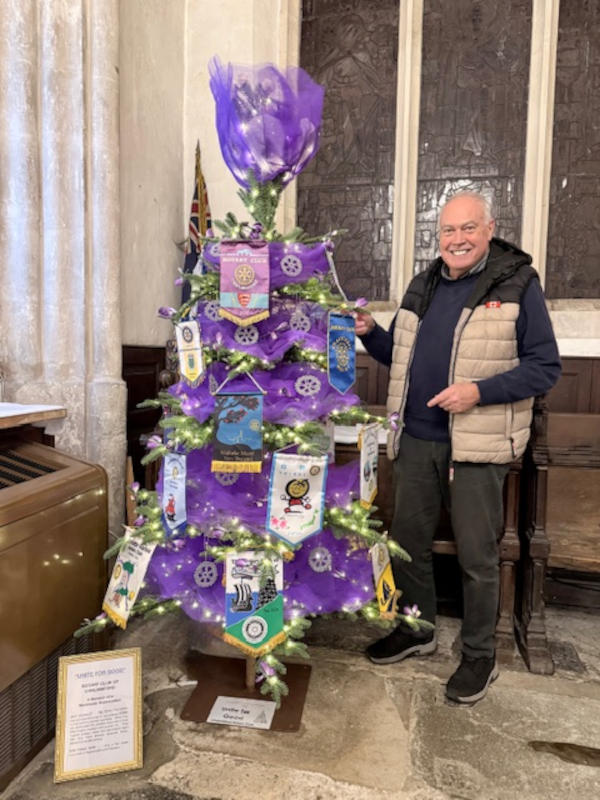 A smiling man standing next to a Christmas tree ddcorated in purple