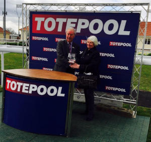 Two people standing at a Totepool dest and banner
