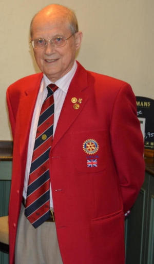 Smiling bald man wearing a red blazer bearing Rotary badges and a Rotary tie