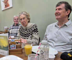 Three informally dressed people sitting one side of a long dining table