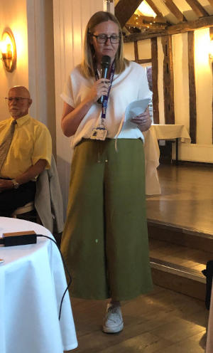 A long-haired lady wearing glasses and holdina a microphone