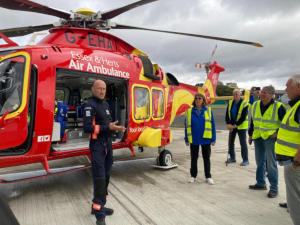 People, most wearing yellow hi-viz jackets, looking at a red air ambulance