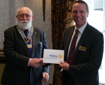 A bearded man wearing a chain of office handing a white plaque to another man