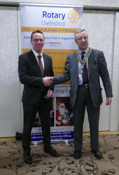 Two men shaking hands in front of a Rotary banner