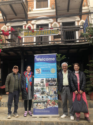 Four people standing with a Rotary pull-up banner in front of a building with a balcony