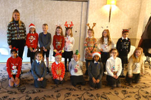 A teacher and smiling junior school children in Christmas jumbers