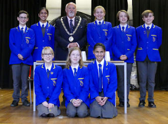 A bearded man wearing a chain of office standing in the middle of secondary school children wearing blue uniforms