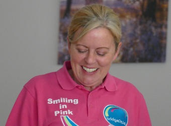 A smiling blonde woman wearing a pink T-shirt