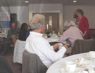 People at dining tables listening to a lady speaking