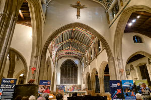 The inside of a cathedral with a grand piano in front of the altar, Rotary banners one either side and an audience