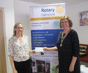 Two smiling ladies in front of a Rotary banner, one handing a cheque to the other
