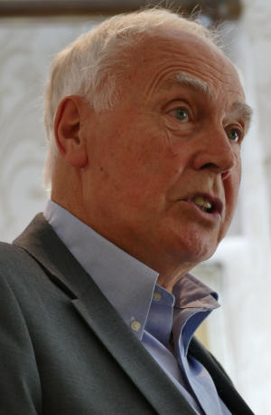 A white-haired man wearing an open-necked blue shirt