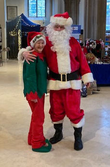 A woman dressed as an elf with Santa in a large church building