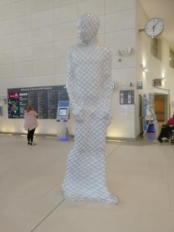 A large white stylised human figure in a large space in a building