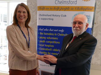 A woman and a man shaking hands in front of a Rotary pull-up banner