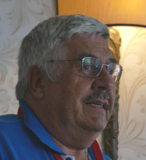 A grey-haired man wearing glasses and a blue polo shirt